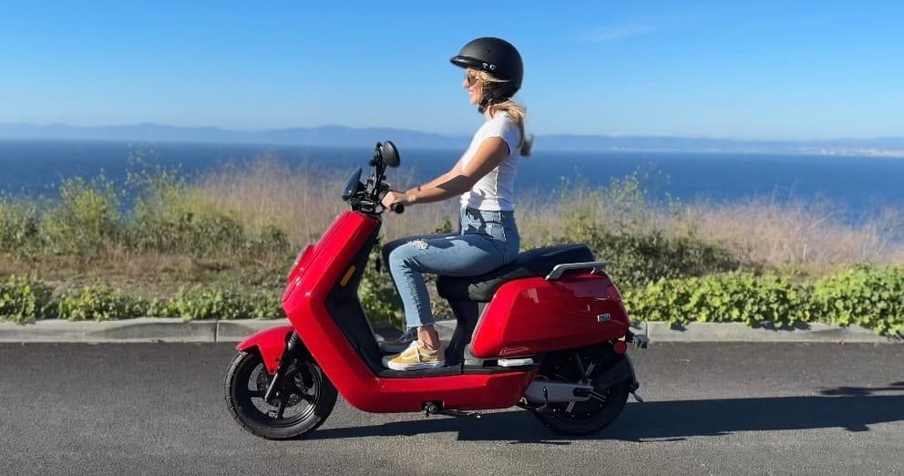 Person riding red electric scooter along coastal road overlooking ocean