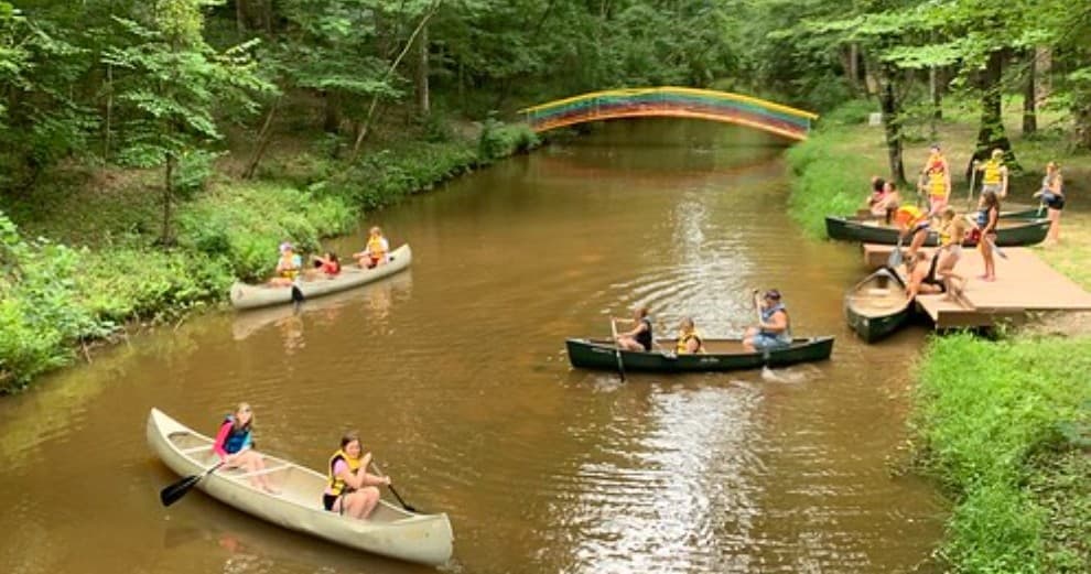 Canoe trip on shaded forest river with campers paddling