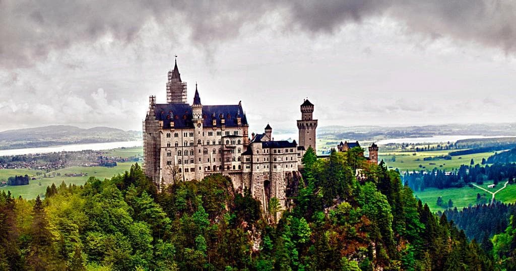 Panoramic castle perched on hill with dramatic sky and forests