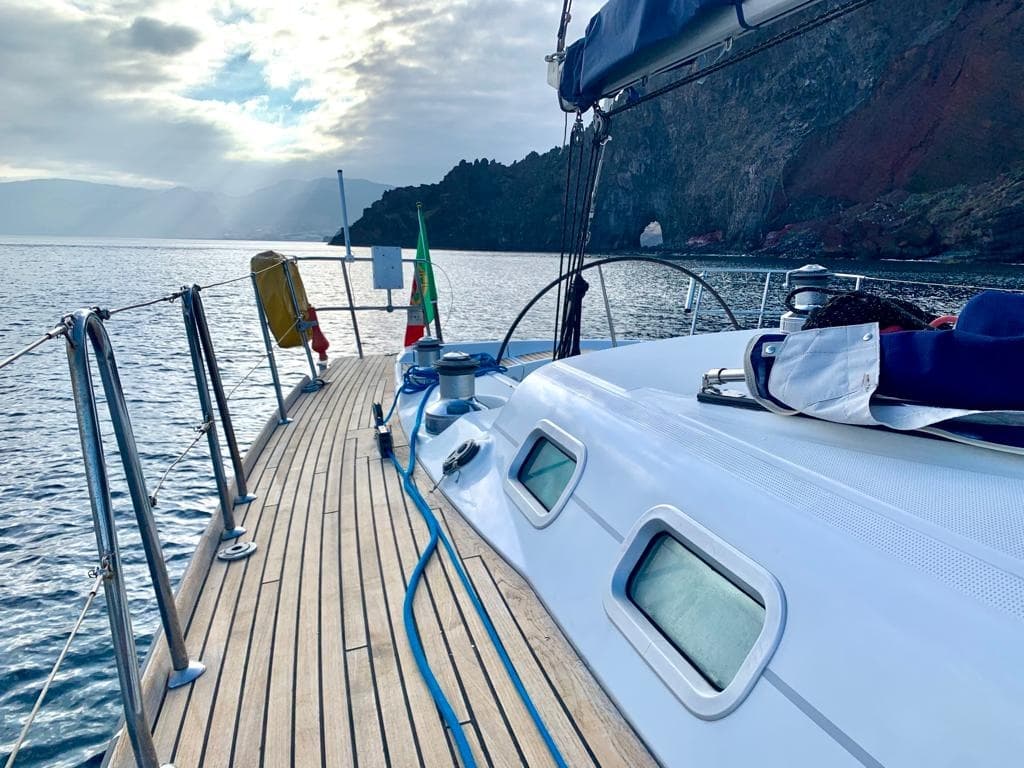 Sailboat teak deck approaching rocky coastline at sunset