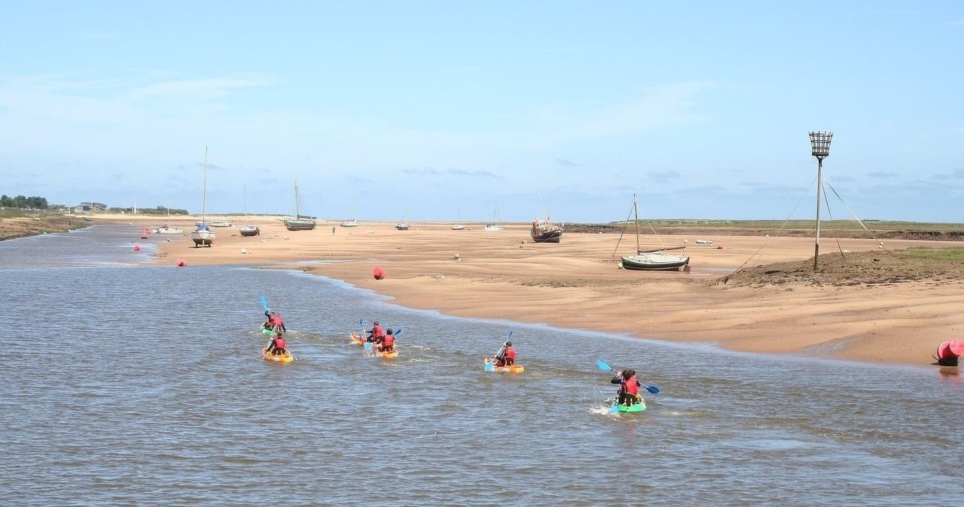 Kayakers paddling along sandy estuary shoreline under blue sky