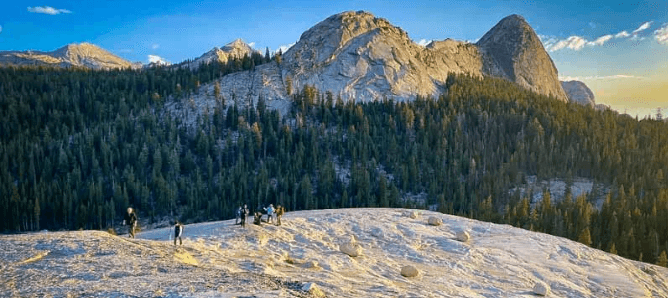 Granite ridge hikers with sweeping mountain forest vista at sunrise