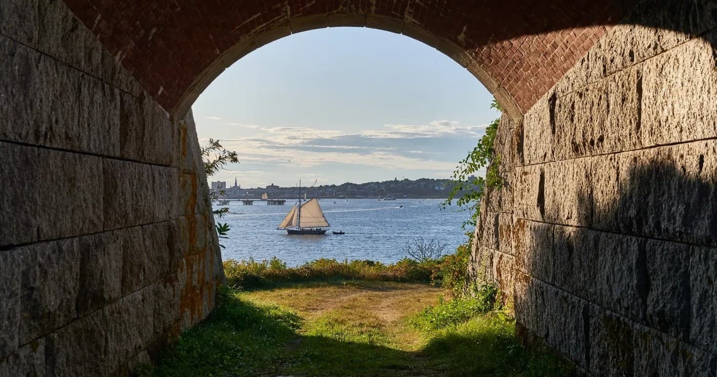Stone arch framing ocean view toward lighthouse on coastal inlet