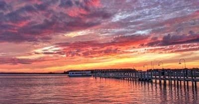 Vibrant sunset over coastal pier and calm bay, scenic waterfront