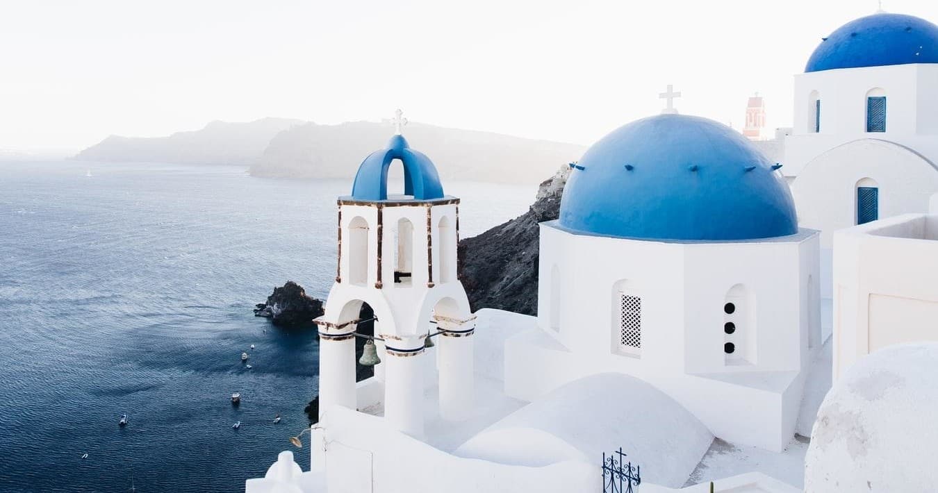 White-washed Santorini chapel with blue domes overlooking caldera
