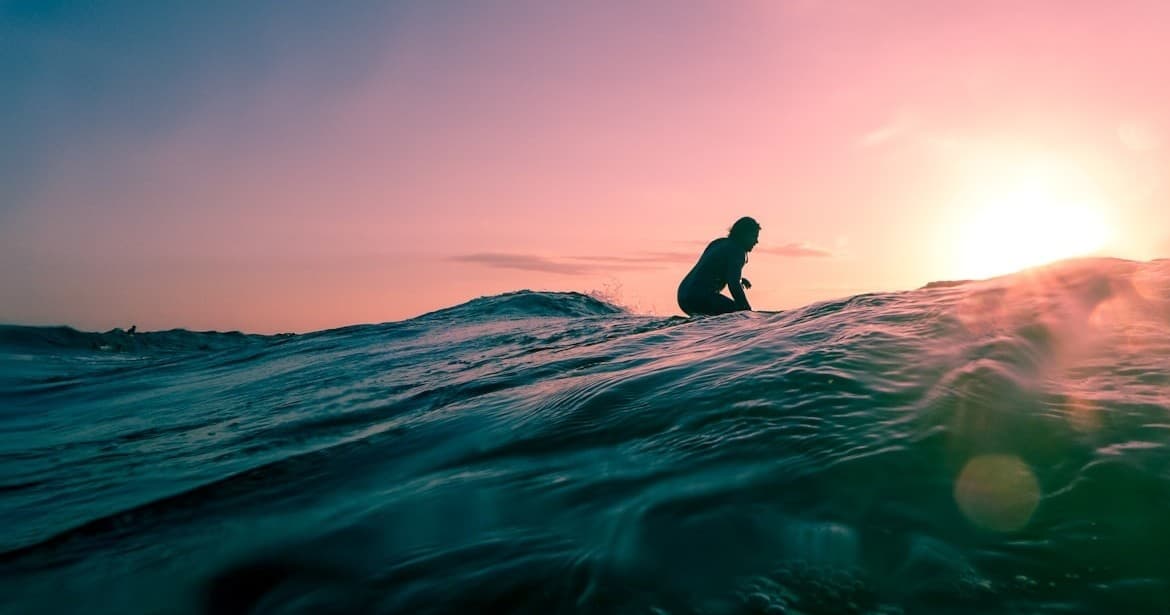 Surfer sitting on board at sunrise with colorful ocean sky