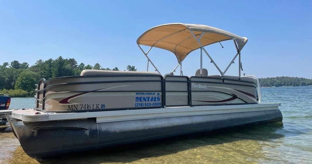 Side view pontoon cruising shallow lake with tan bimini top