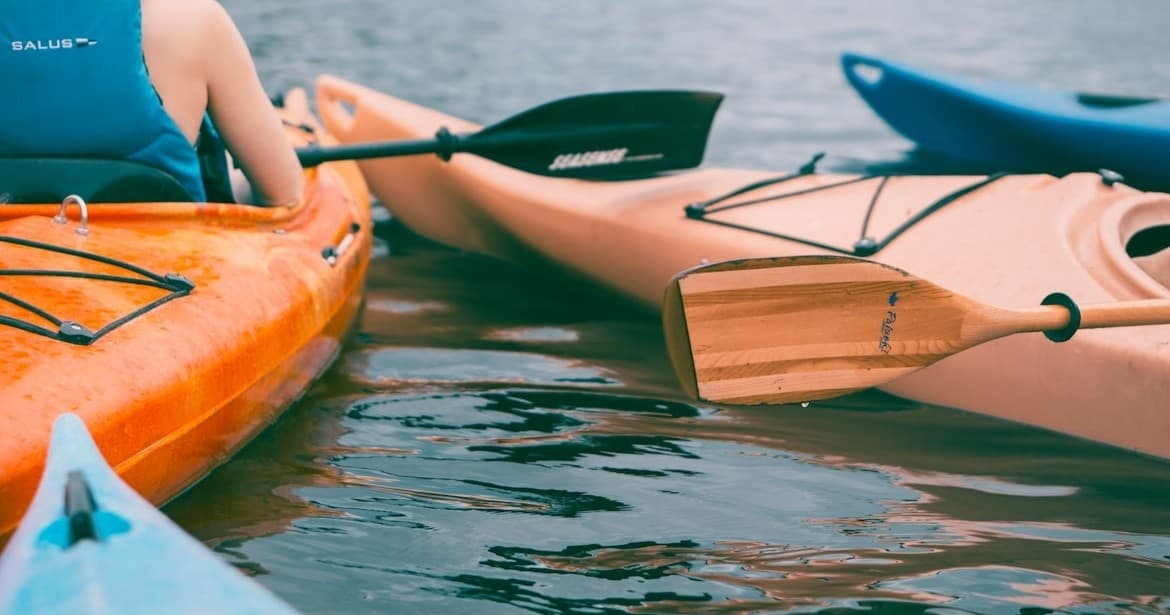 Colorful kayaks close up on reflective water, adventure tour prep