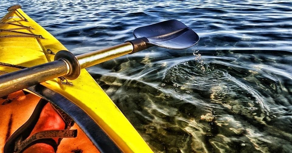 Yellow kayak bow and paddle gliding over clear rippling water