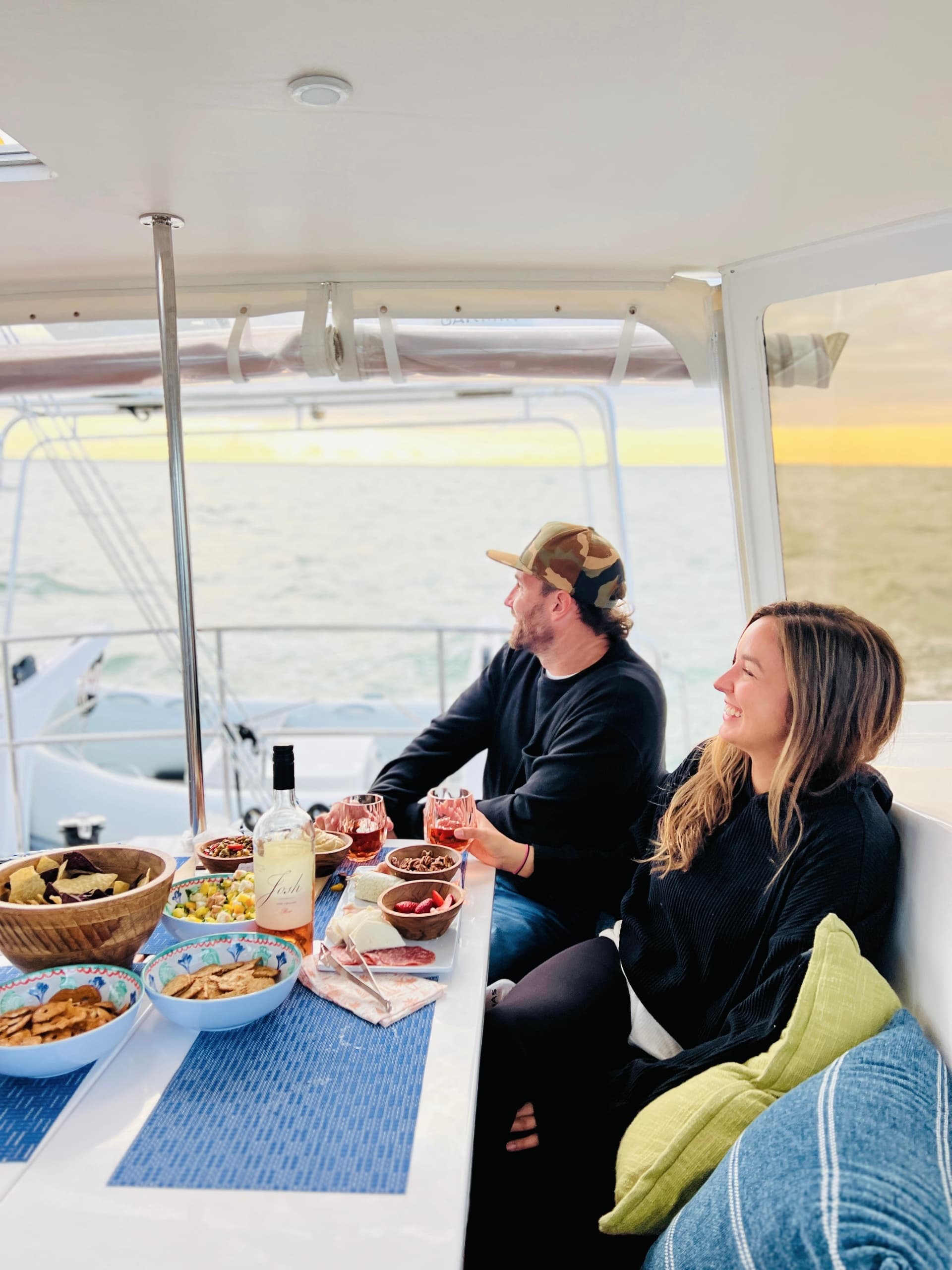 Couple dining aboard catamaran in covered cockpit at sunset cruise