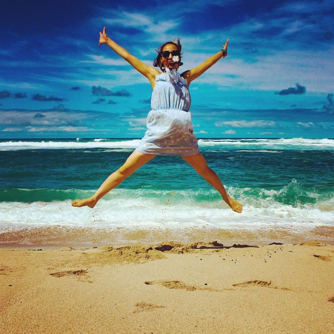Woman jumping joyfully on sunlit tropical beach with waves