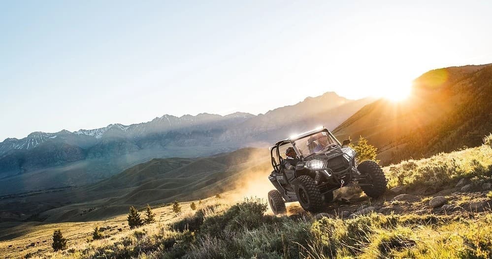 UTV off-road riding across sunlit mountain meadow at sunset