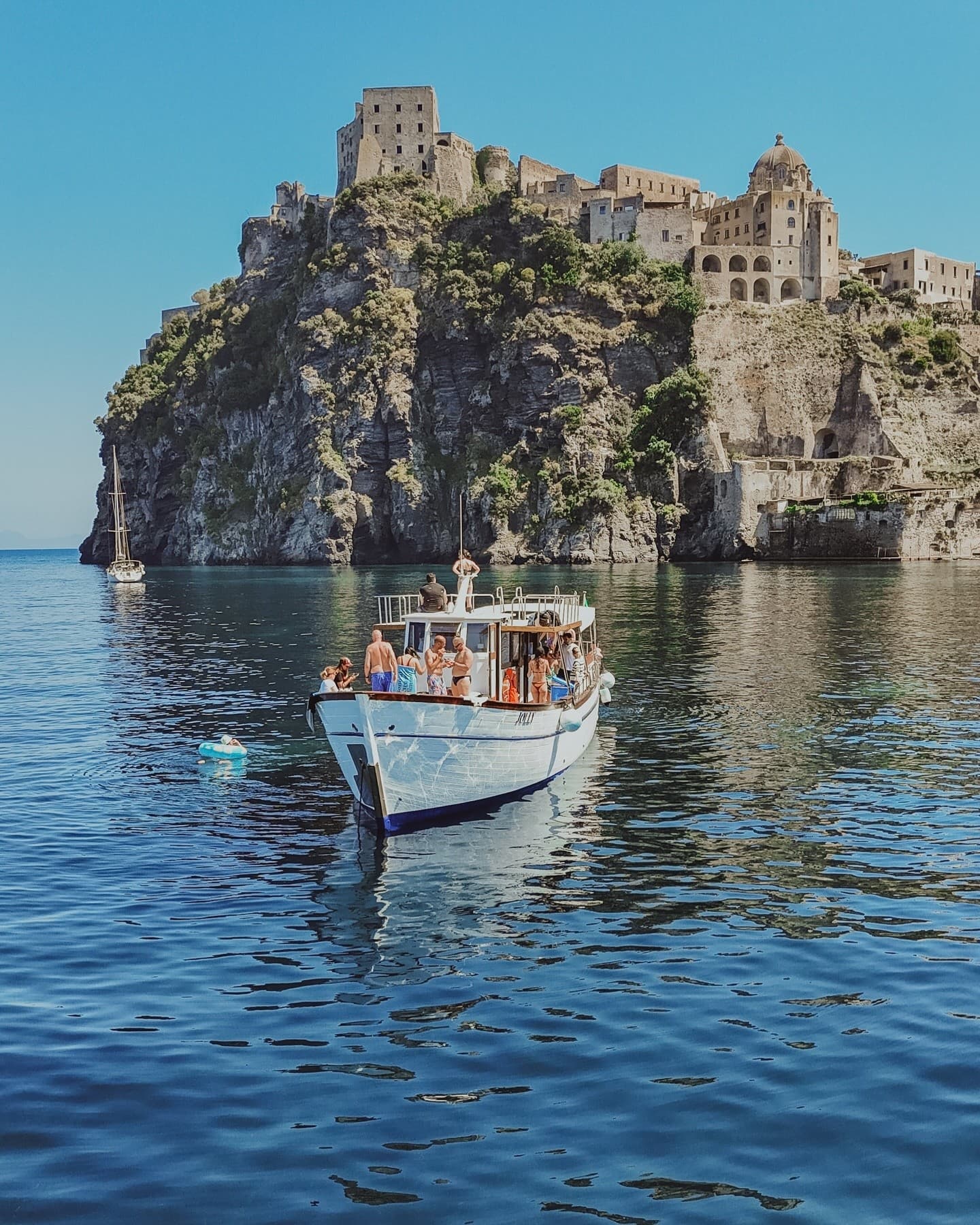 Small motorboat cruising beneath dramatic coastal cliffs near Ischia