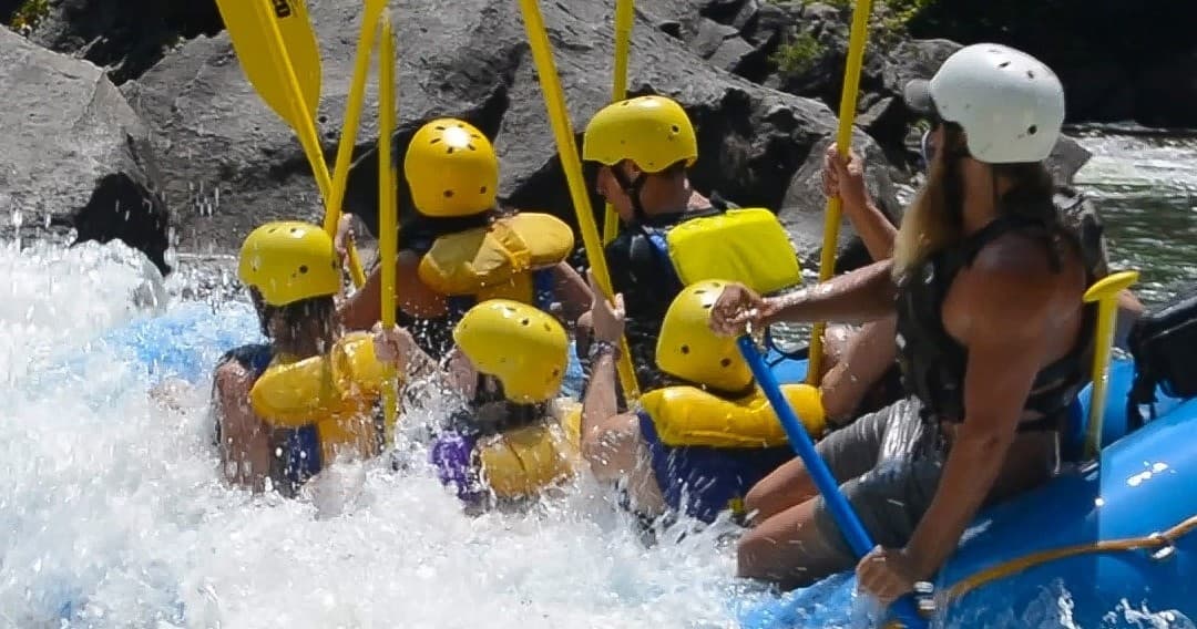 Whitewater raft team in helmets paddling through big river waves