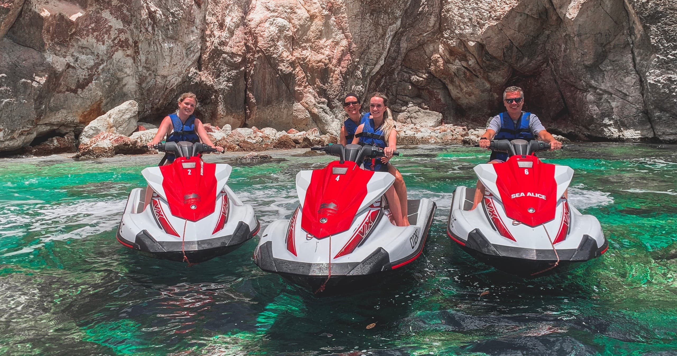 Three jet skis anchored in rocky cove for group sea tour