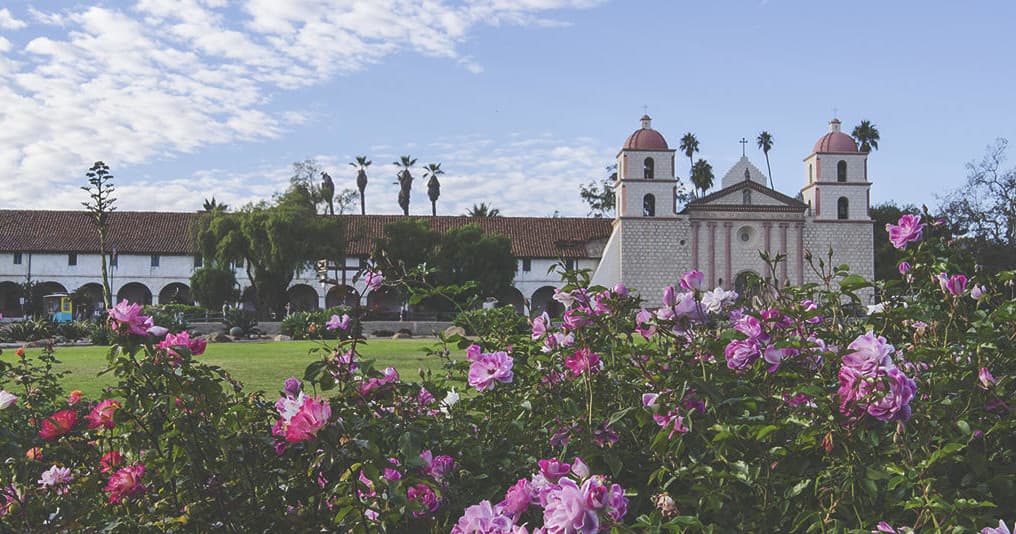 Historic California mission garden with visitors exploring grounds