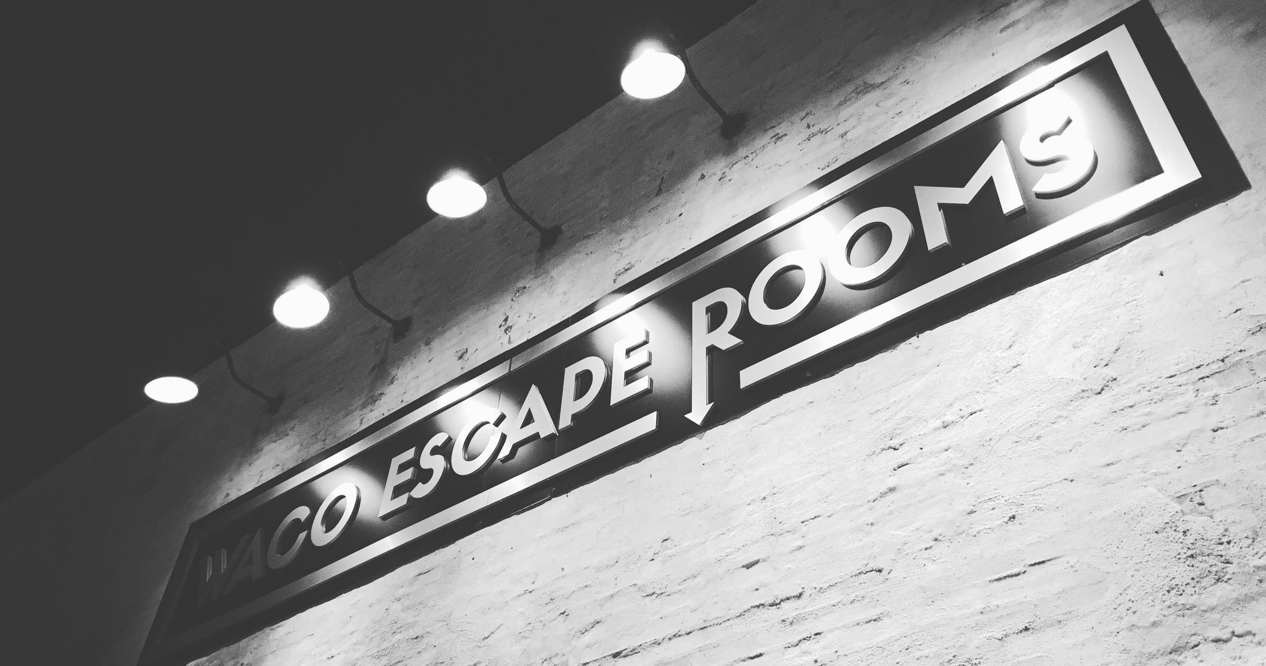 Black-and-white angled sign reading Waco Escape Rooms on exterior wall
