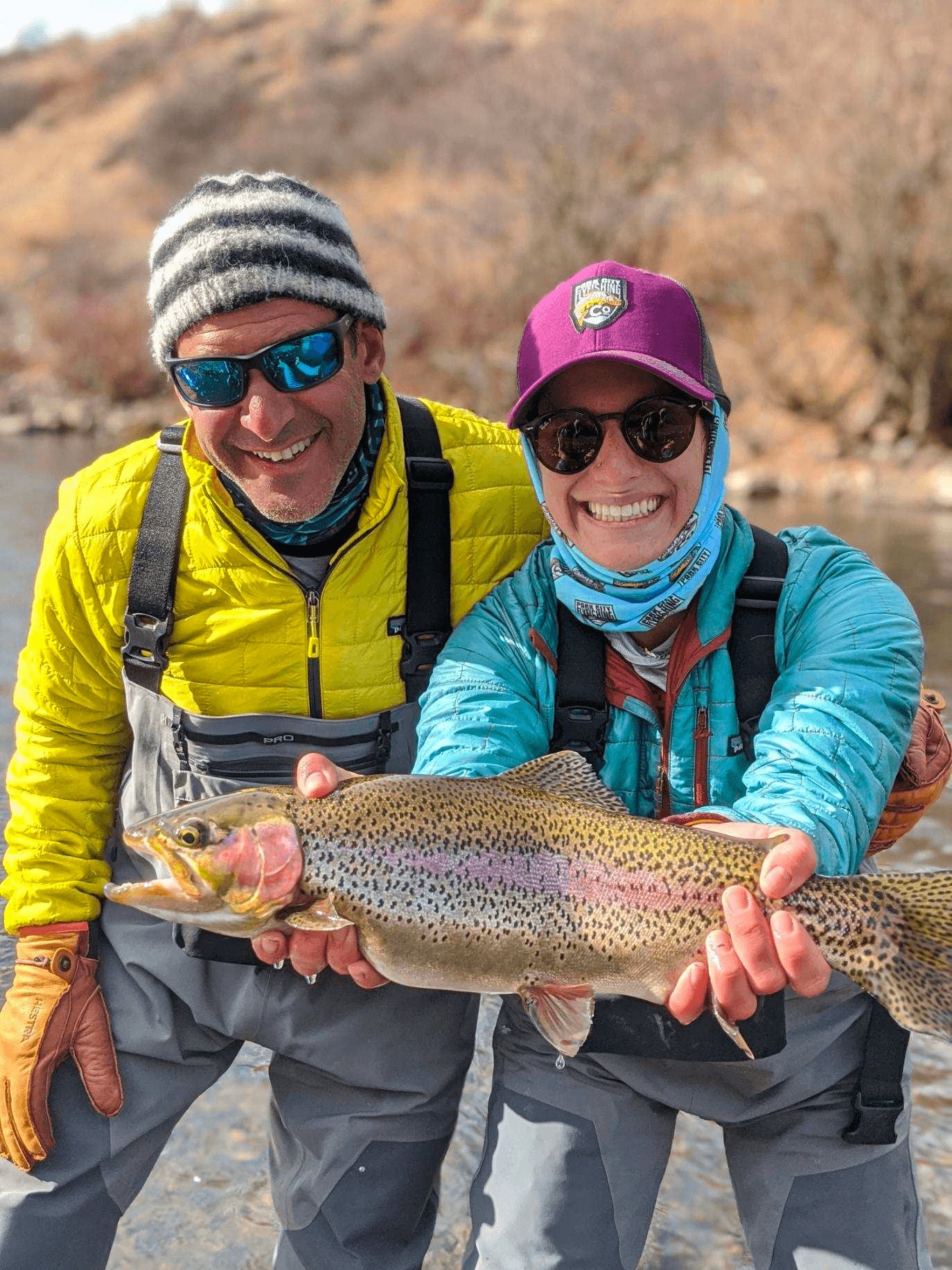 Guide and client holding trophy rainbow trout by riverbank