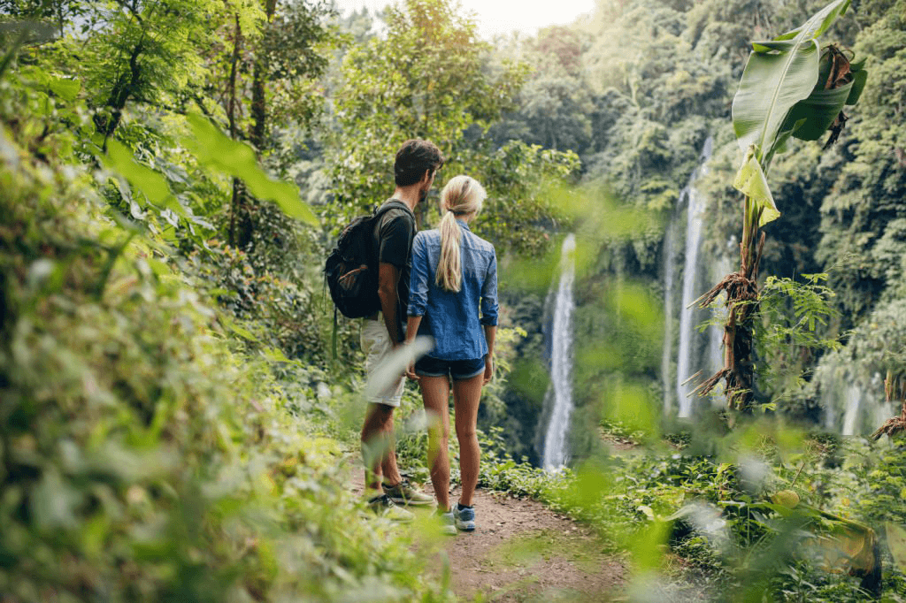 Couple hiking on lush trail toward tropical waterfall in rainforest