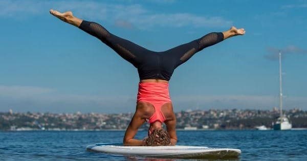 Woman balancing in headstand on paddleboard over calm bay waters