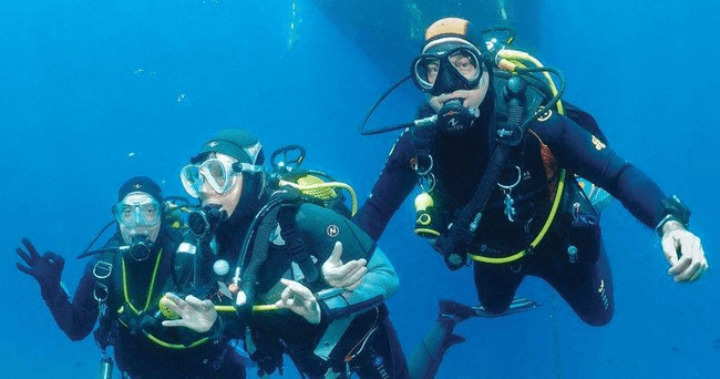 Three scuba divers exploring turquoise open water with bubbles