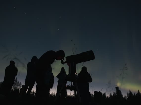 Silhouetted stargazers using a telescope under dark Arctic sky
