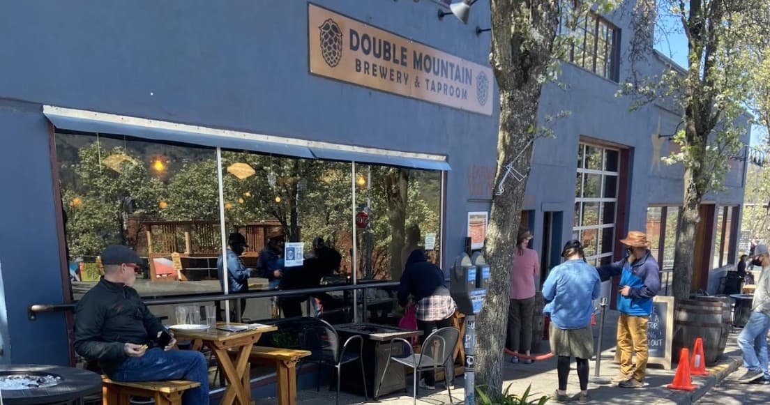 Outdoor brewery patio with people queuing and tables