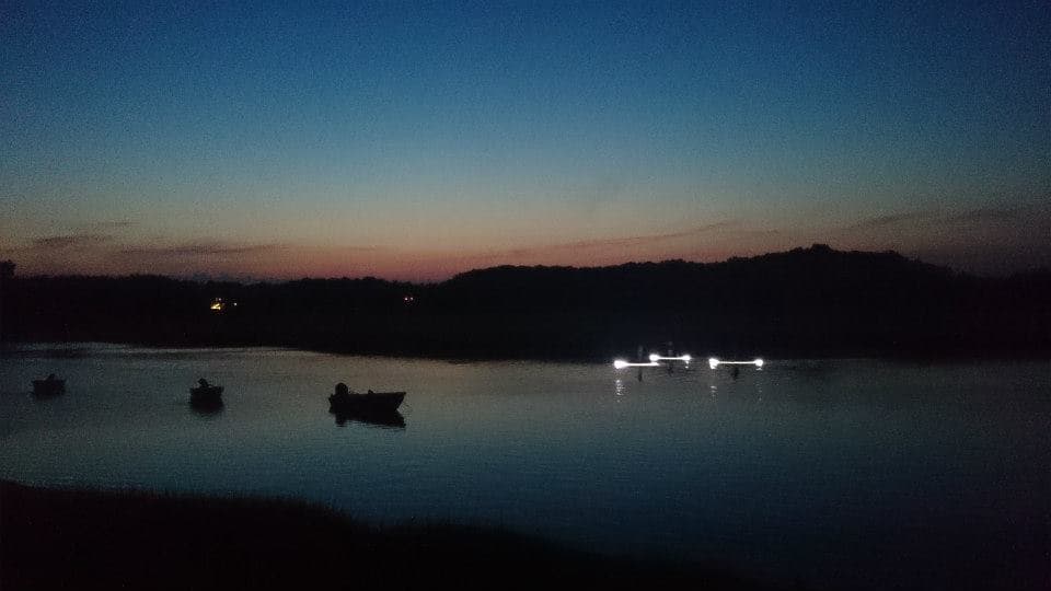 Twilight boats anchored on calm bay with shoreline lights