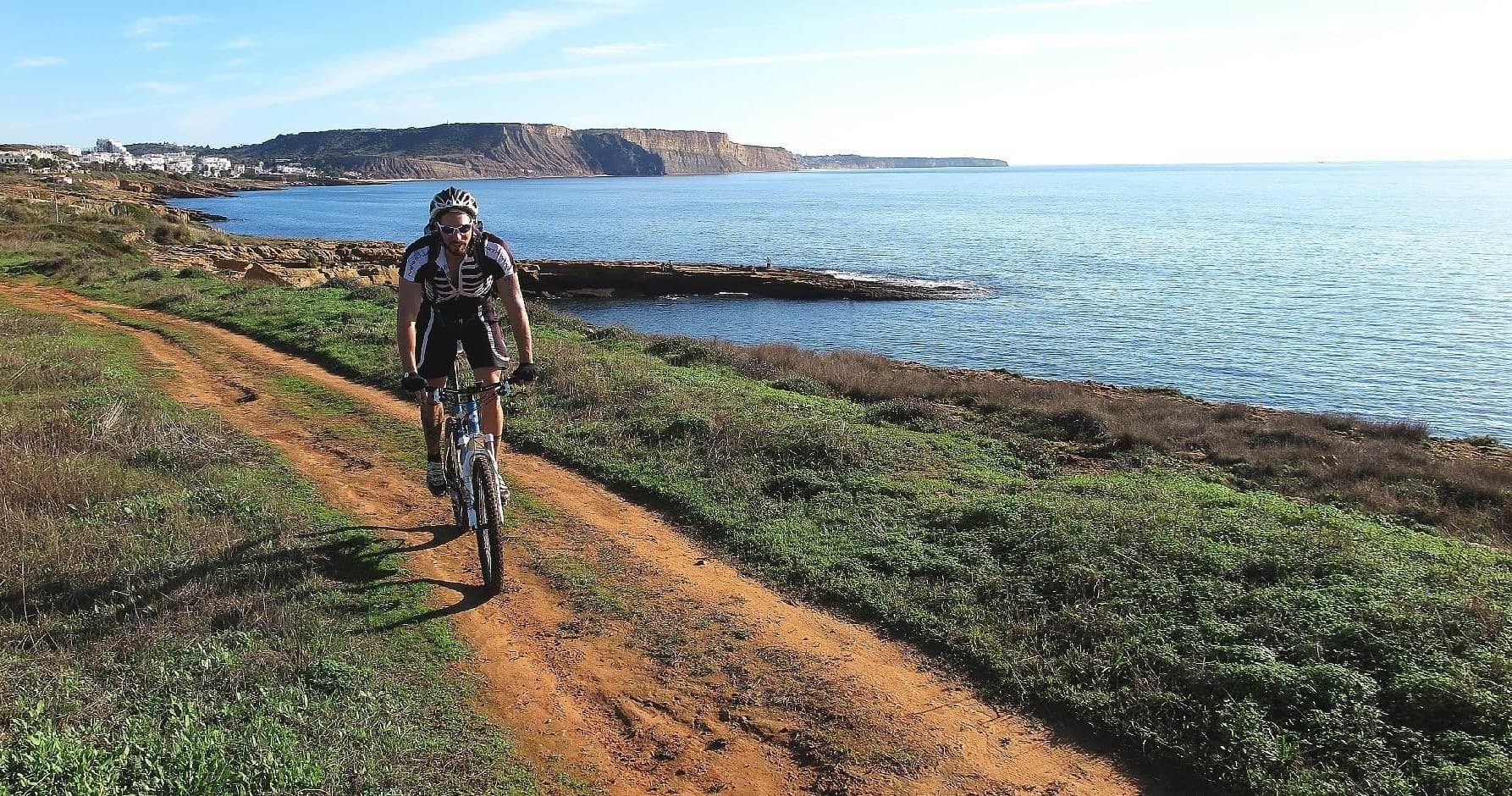 Cyclist riding coastal dirt trail with ocean cliffs in Algarve