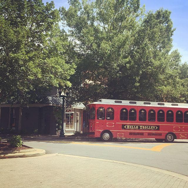 Red trolley parked under trees at suburban curb for neighborhood tour