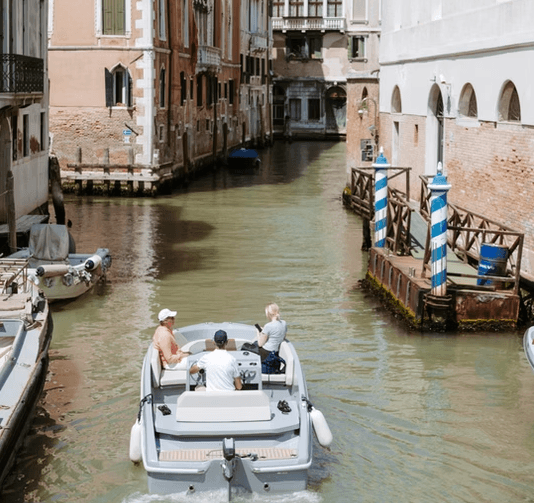 Tourists aboard motorboat navigating narrow Venetian canal