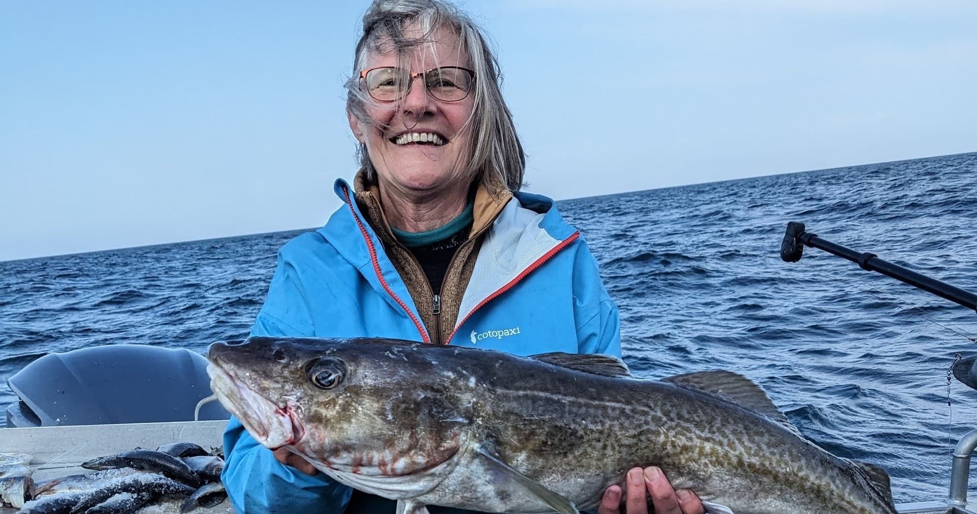 Angler woman holding large cod on ocean charter near Alaska coast