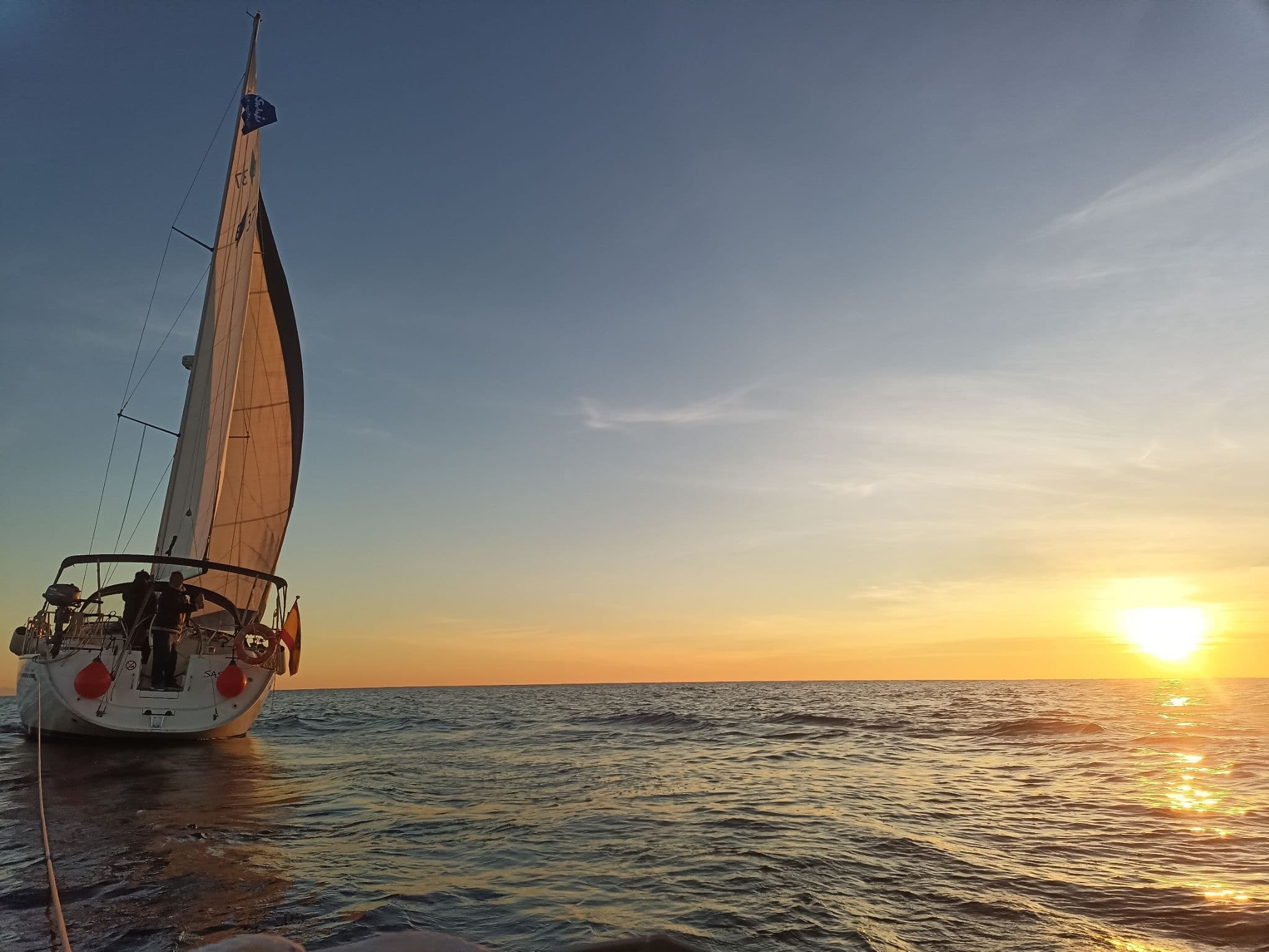 Sailboat cruising at sunset on open sea near horizon