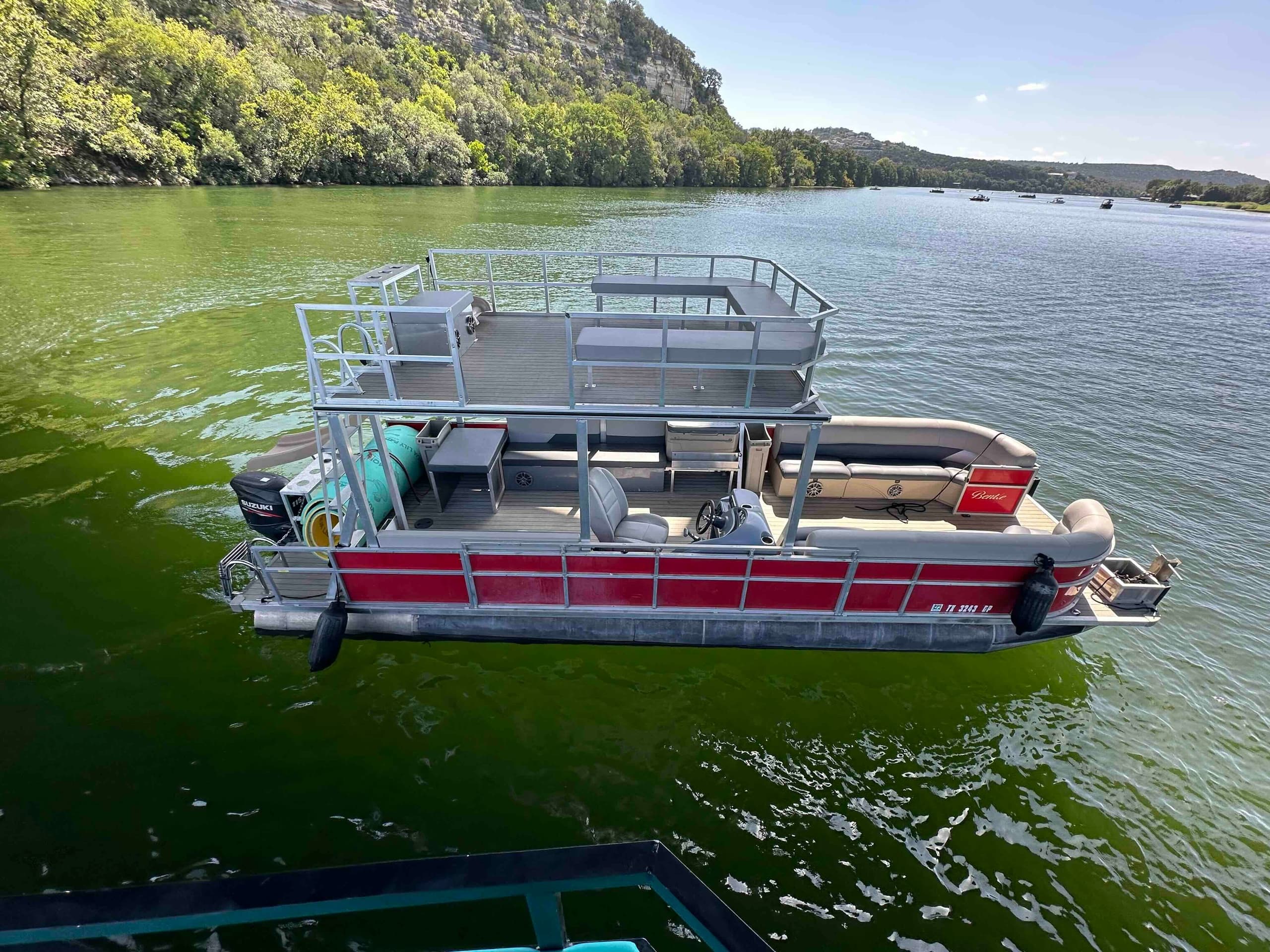 Aerial red pontoon cruising near shoreline on green lake