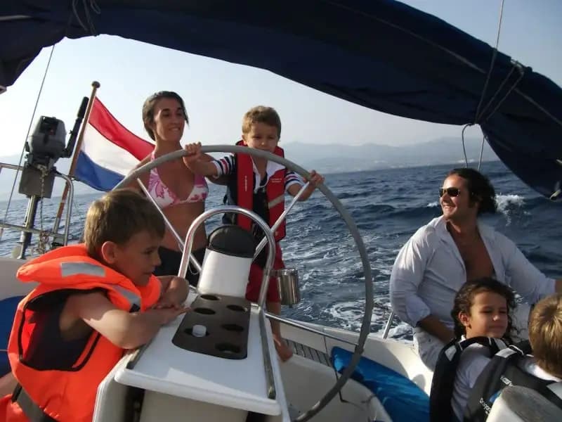 Family sailing on yacht in open sea enjoying helm and kids