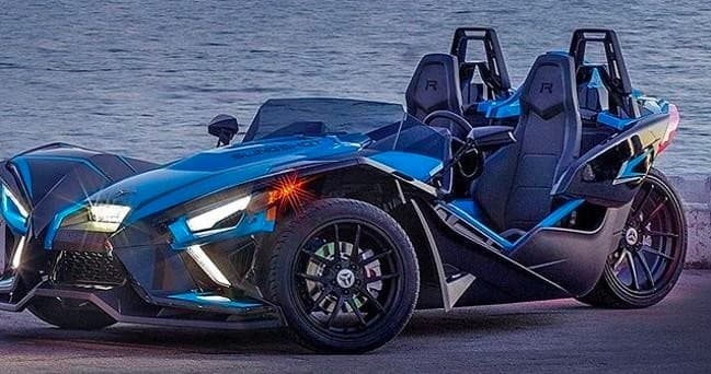 Blue Slingshot parked by waterfront at sunset, coastal tour