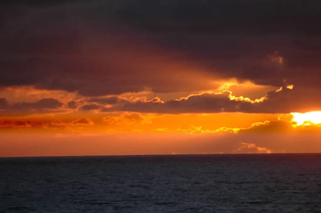 Vivid orange sunset over ocean with coastal kayaking scene