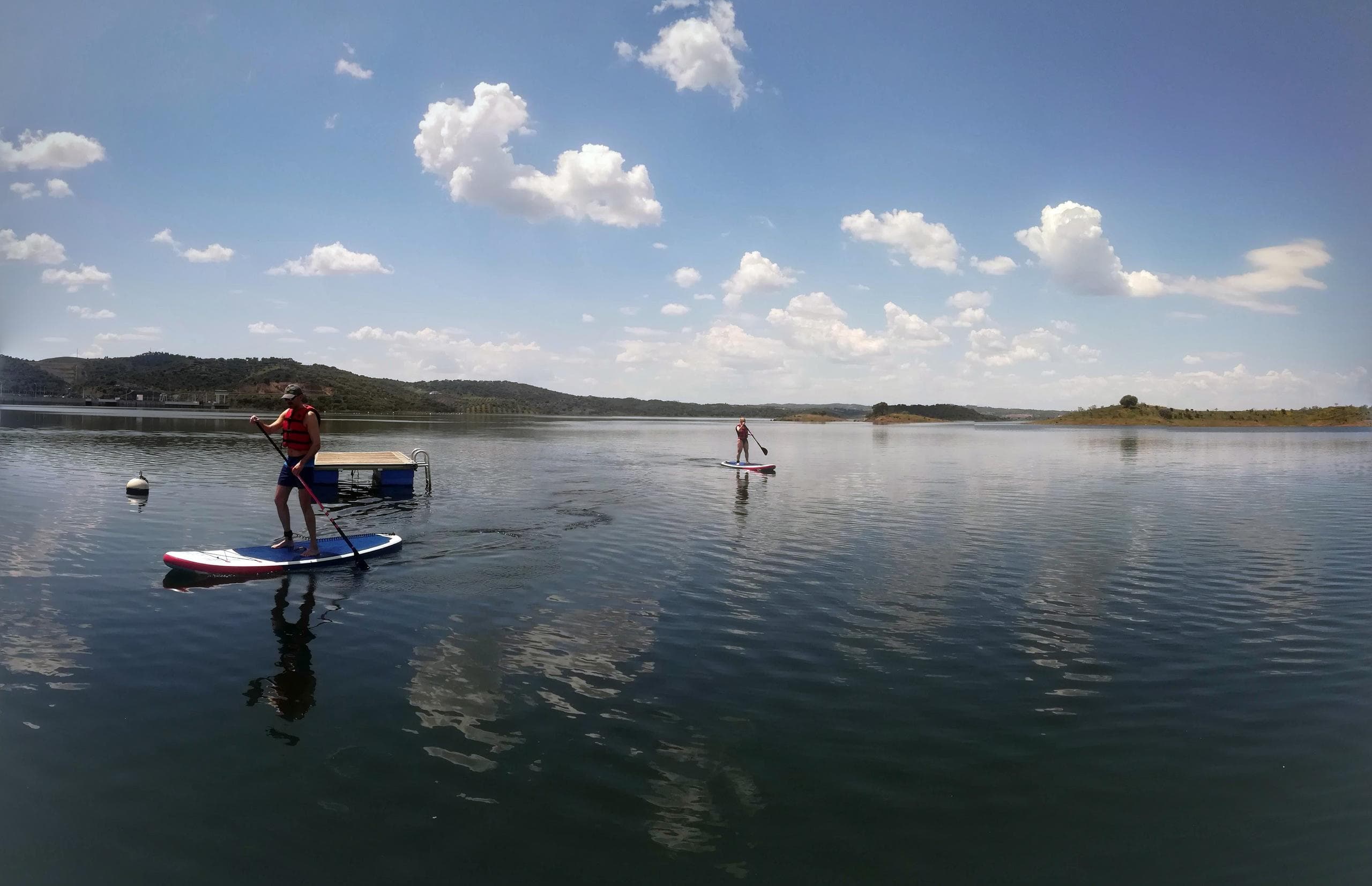 Paddleboarders gliding across reflective calm lake at midday