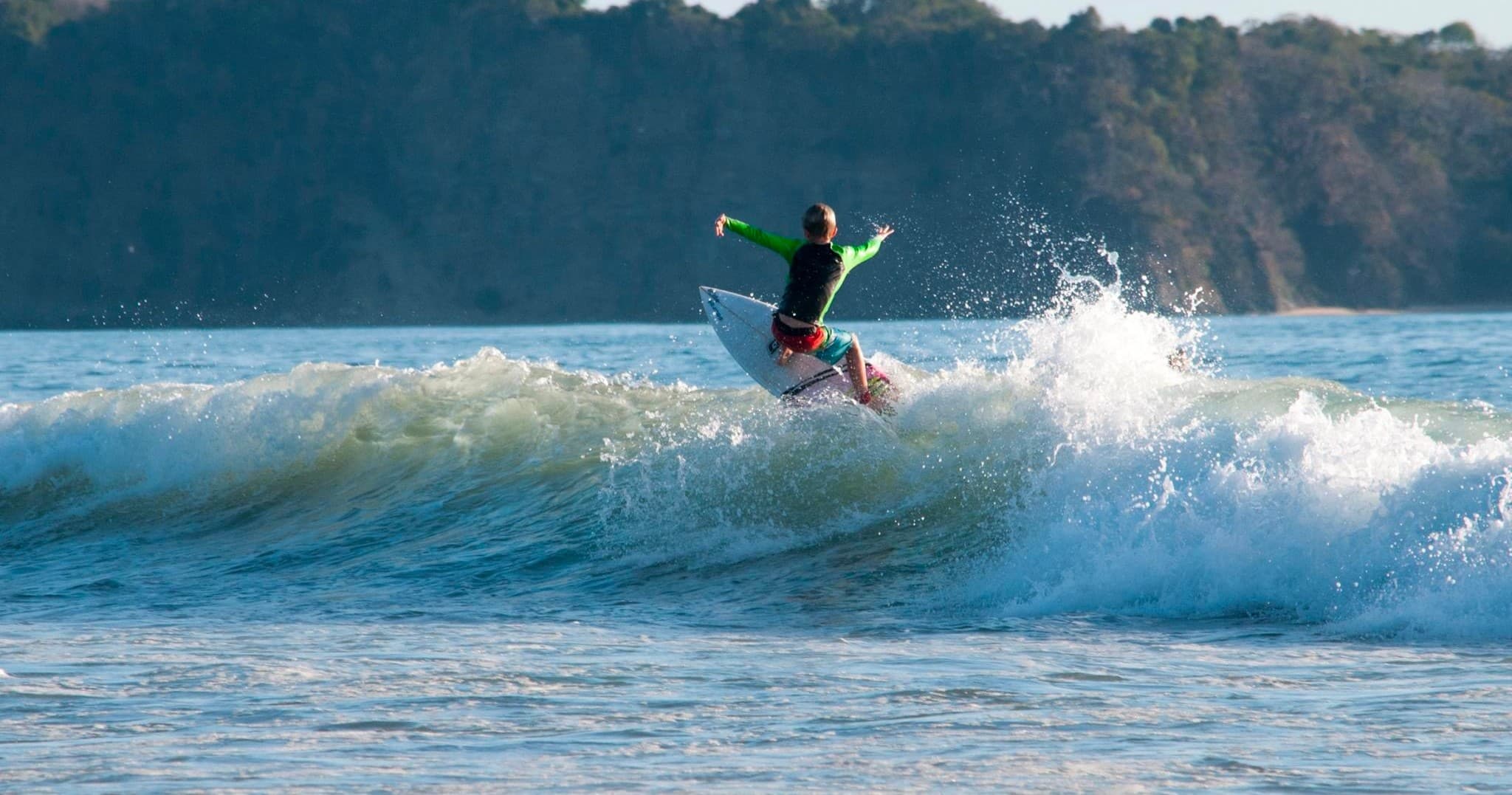 Surfer carving a turn on blue wave near rocky shoreline