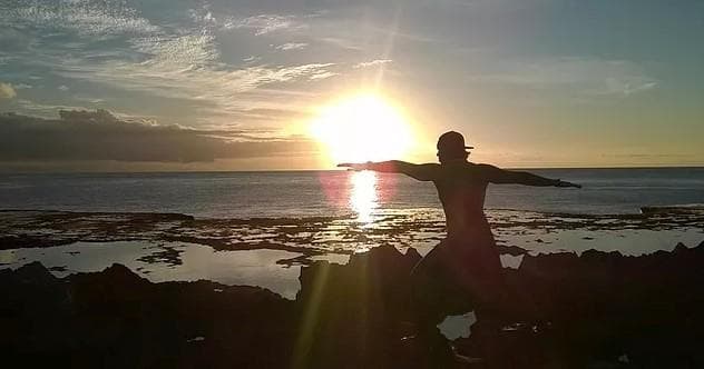 Sunset silhouette stretching on lava rocks by the ocean