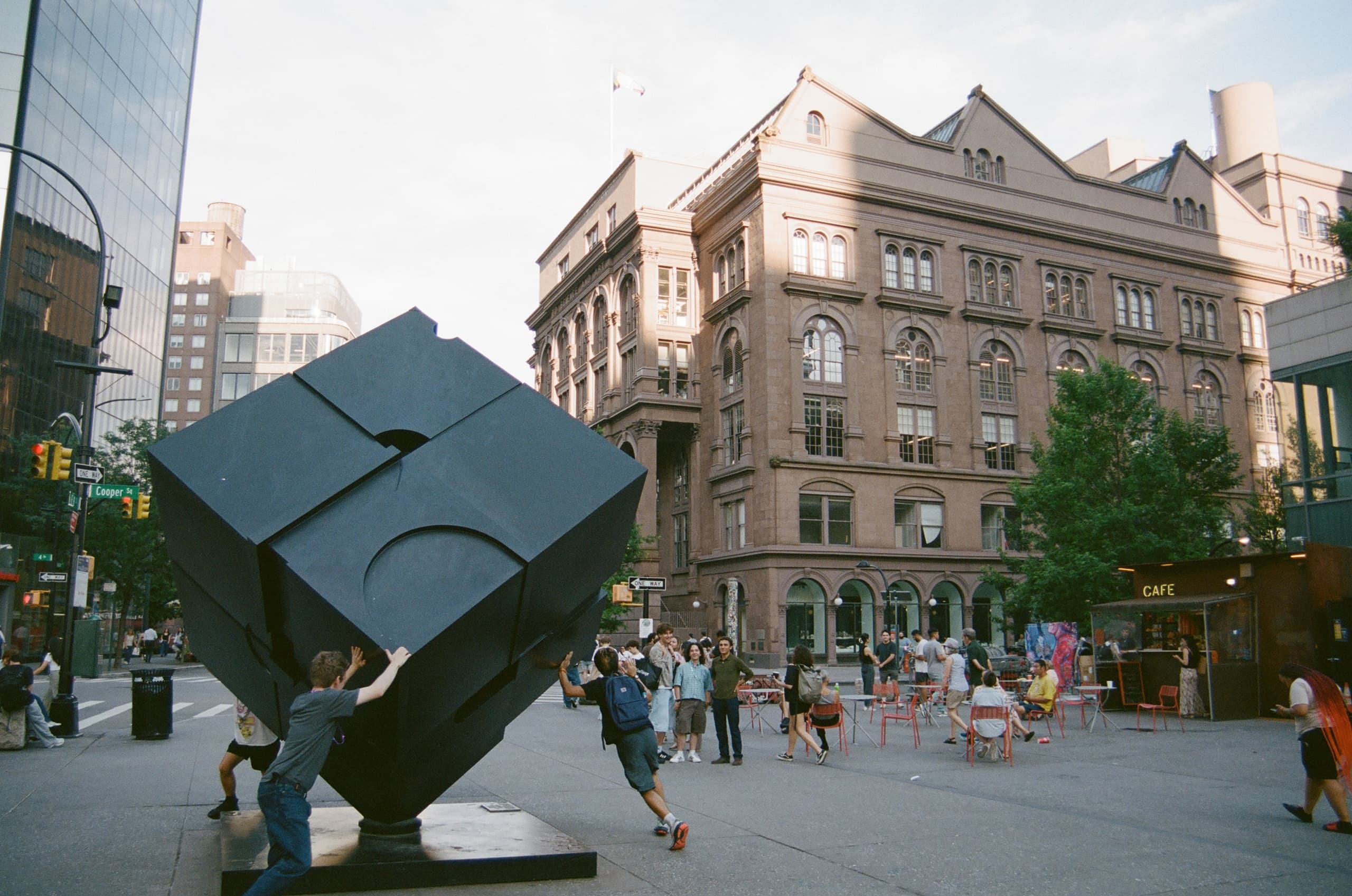 Black cube sculpture in outdoor Manhattan plaza with pedestrians