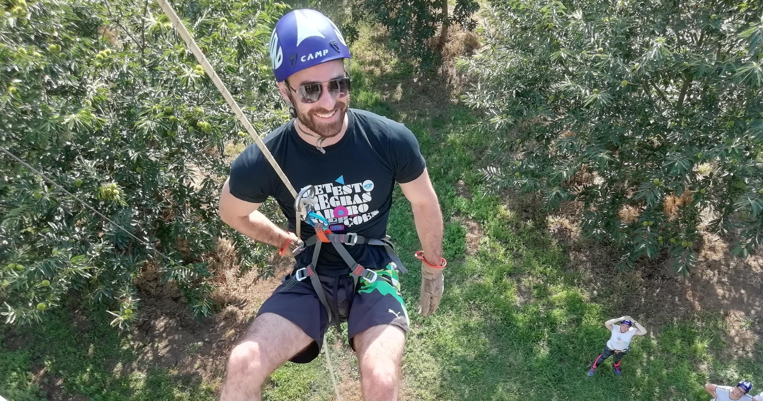 Man abseiling down rocky cliff through forested canyon