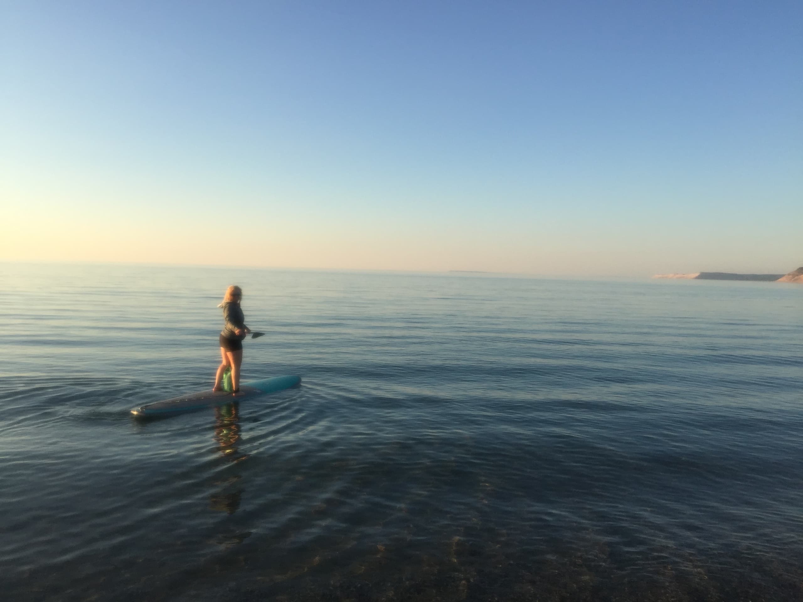 Stand-up paddleboarder on calm open ocean at sunrise
