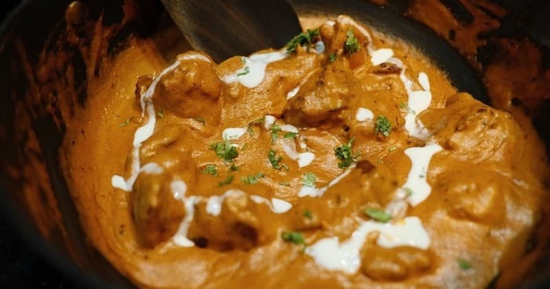 Creamy butter chicken curry simmering in pot, Indian entree