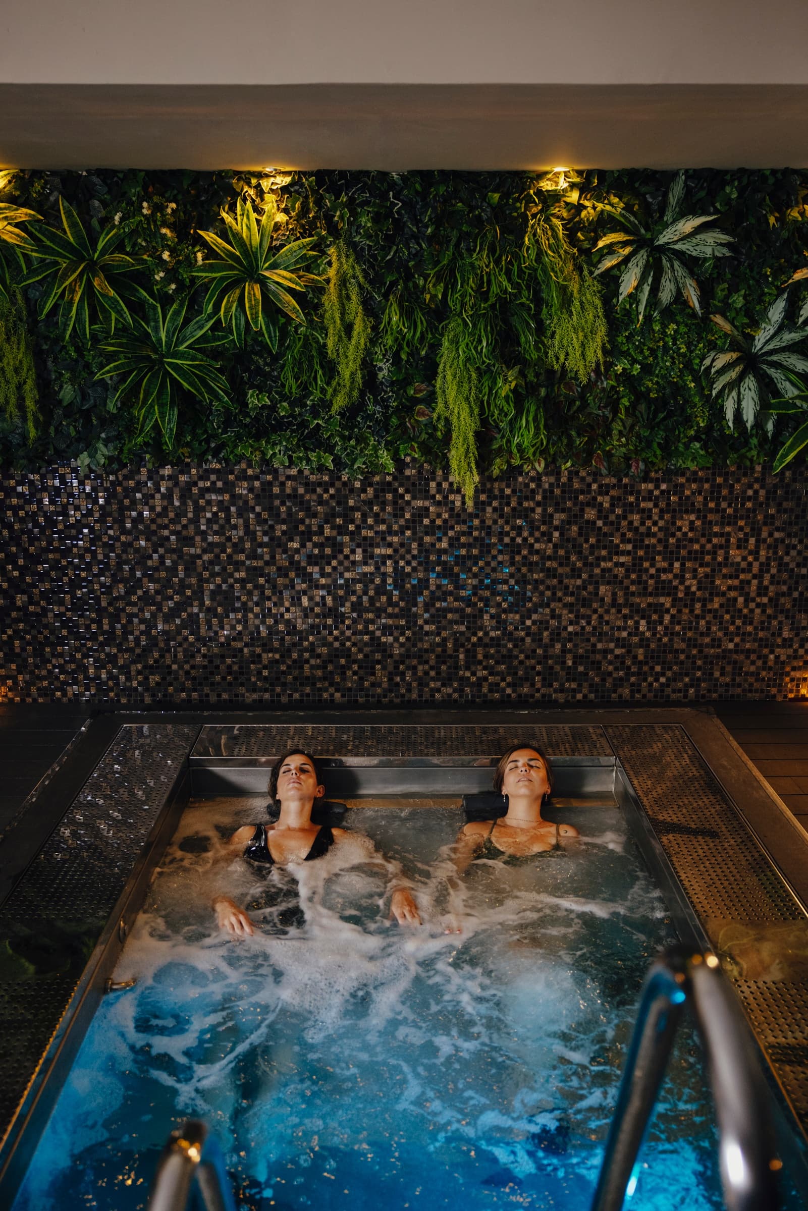Two guests relaxing in indoor spa pool with tropical wall
