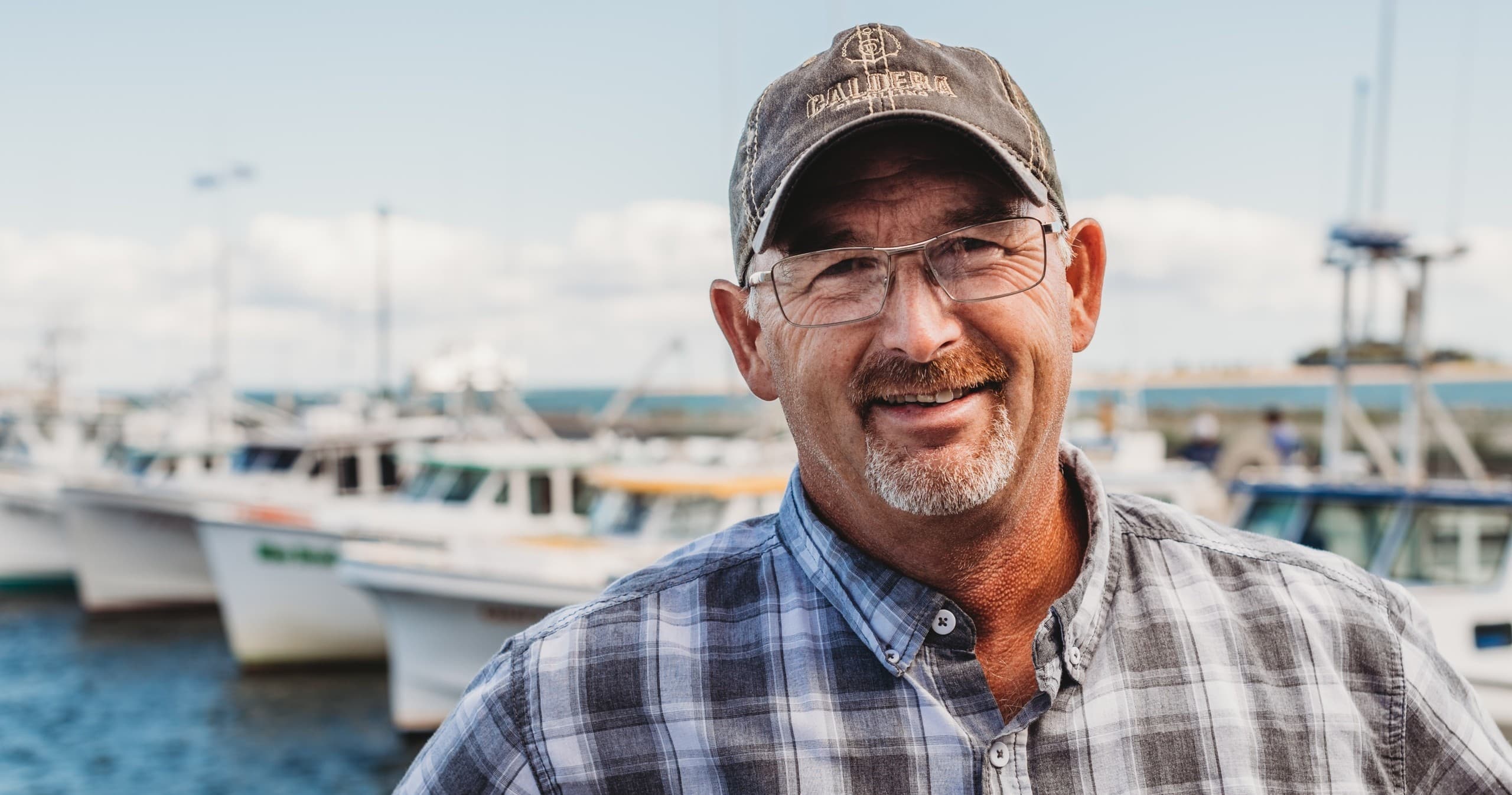 Harbor captain smiling with fishing boats, bright coastal dock