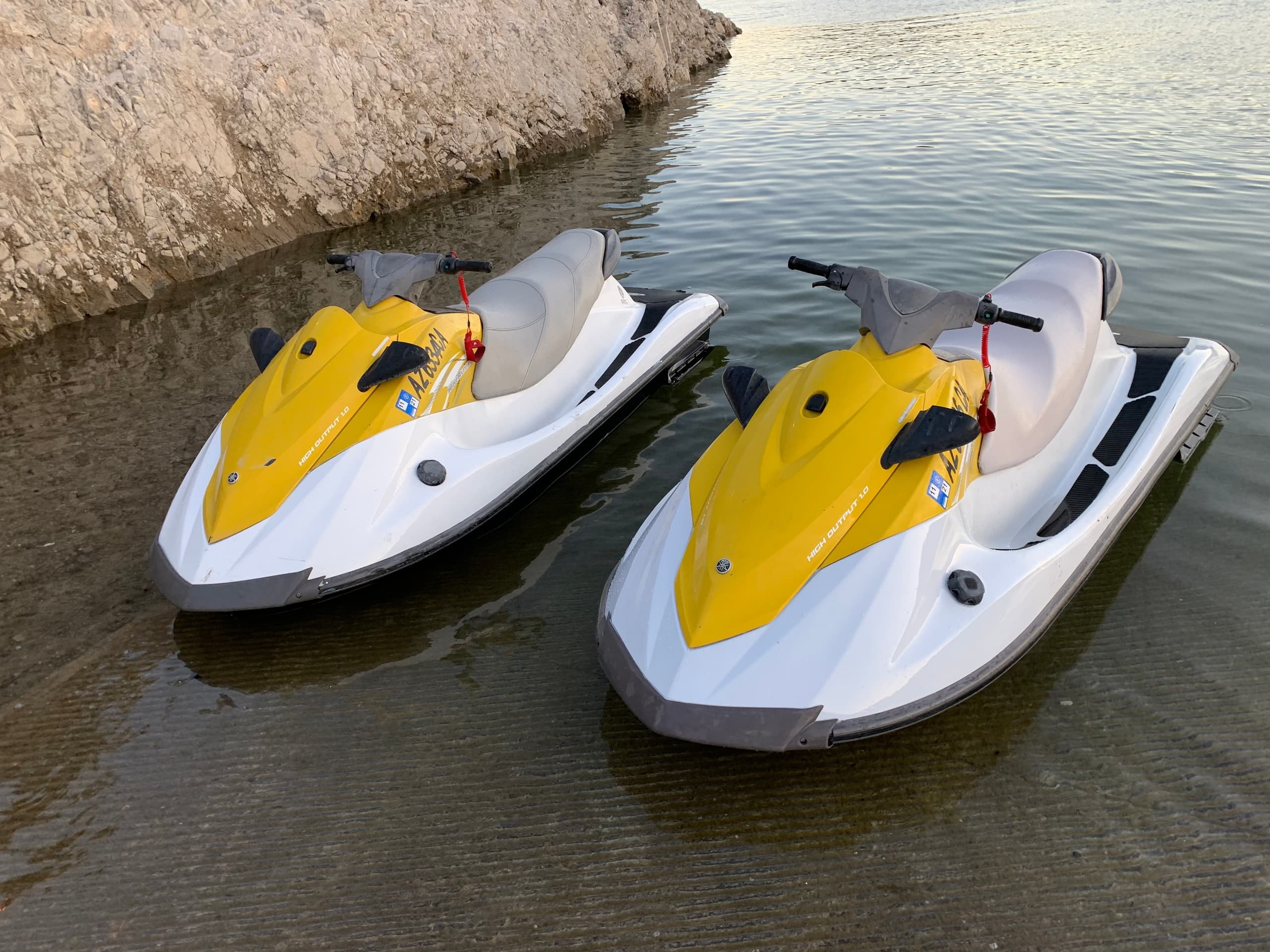 Two yellow jet skis beached in shallow water by rocky shore