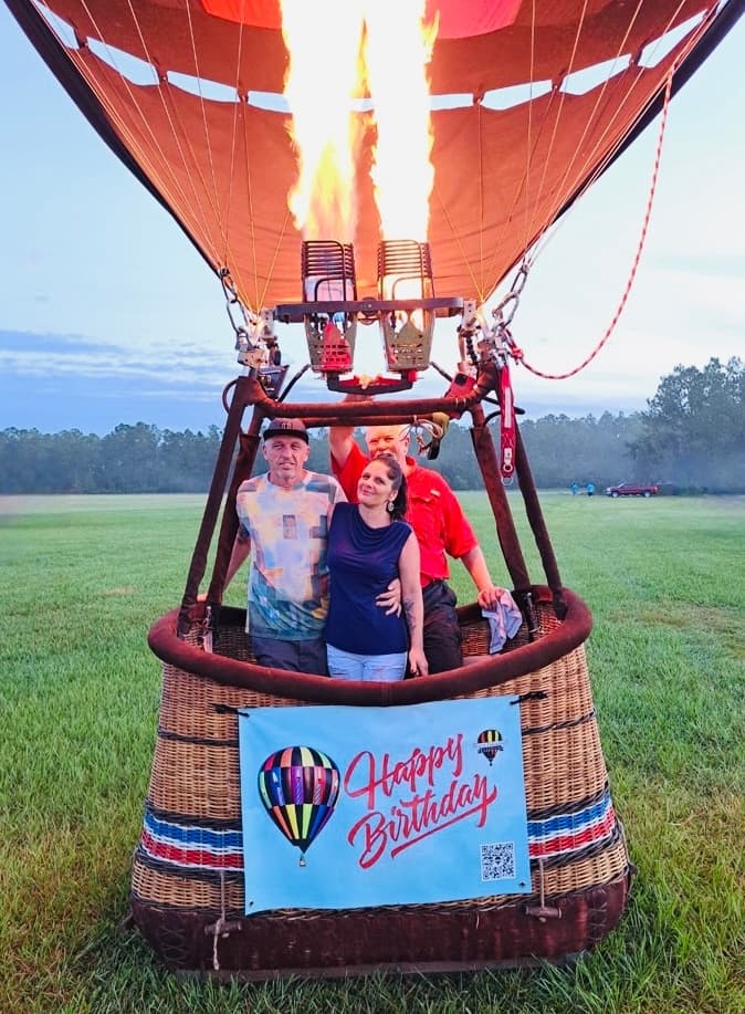 Couple posing in hot air balloon basket with flame above open field
