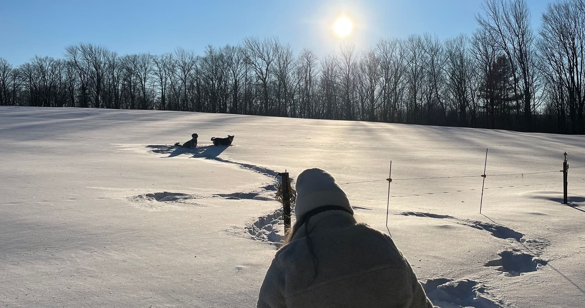 Angler sitting on snowy field drilling ice holes at sunrise