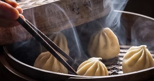 Steaming soup dumplings (xiao long bao) being lifted with chopsticks